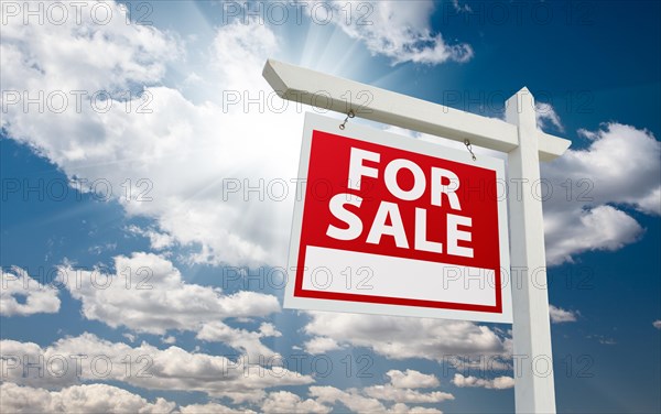 For sale real estate sign over clouds and blue sky with sun rays