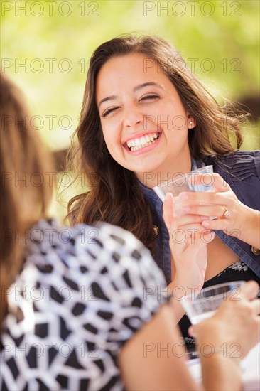 Expressive young adult woman having drinks and talking with her friend outdoors