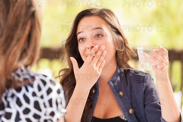 Expressive young adult woman having drinks and talking with her friend outdoors