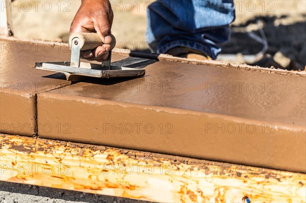 Construction worker using hand groover on wet cement forming coping around new pool