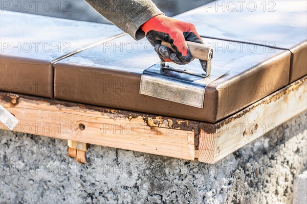 Construction worker using stainless steel edger on wet cement forming coping around new pool