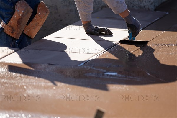 Construction worker smoothing wet cement with hand edger tool