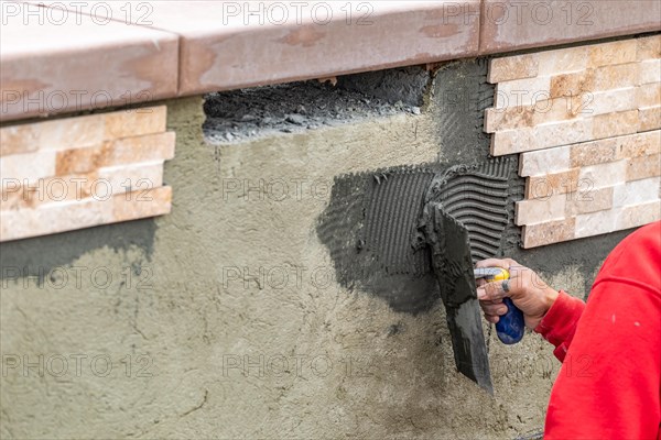 Worker installing wall tile cement with trowel and tile at construction site