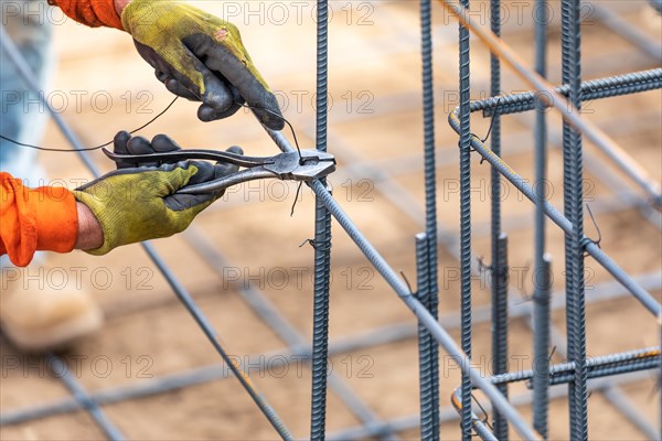 Worker securing steel rebar framing with wire plier cutter tool at construction site