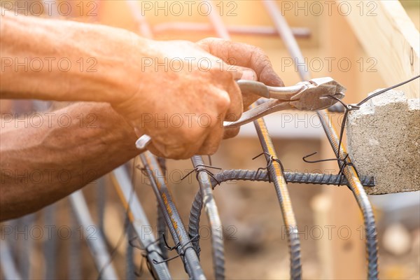 Worker securing steel rebar framing with wire plier cutter tool at construction site