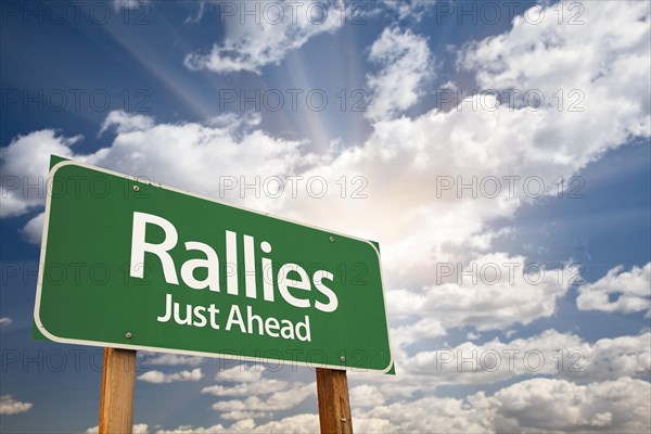 Rallies green road sign against clouds and sunburst