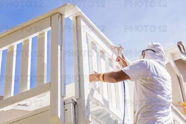 House painter wearing facial protection spray painting A deck of A home