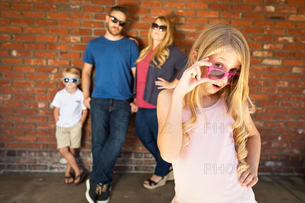 Cute young caucasian girl wearing sunglasses with family behind
