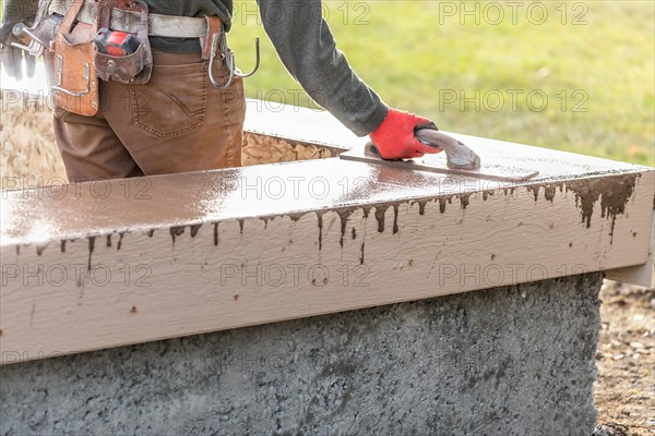 Construction worker using wood trowel on wet cement forming coping around new pool