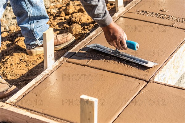 Construction worker using trowel on wet cement forming coping around new pool