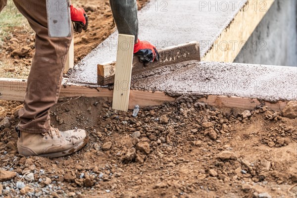 Construction worker leveling wet cement into wood framing