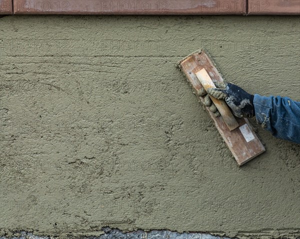 Worker smoothing cement with wooden float at construction site