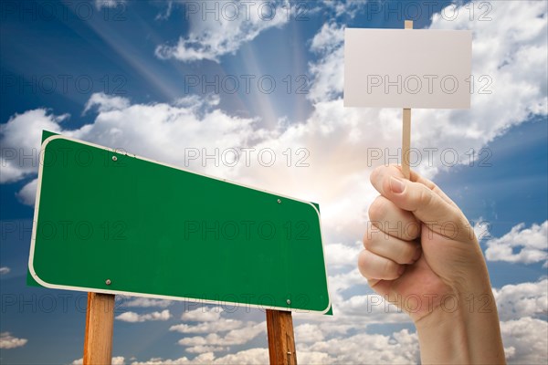 Blank green road sign and man holding poster on stick over blue sky and clouds