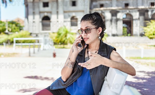 Urban style girl sitting on a bench calling on the phone