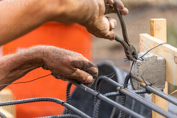 Worker securing steel rebar framing with wire plier cutter tool at construction site