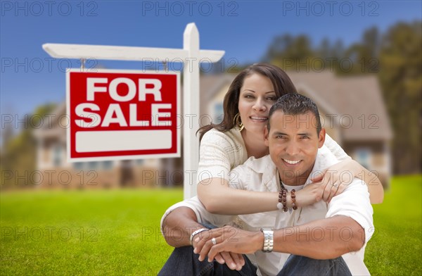 Young happy hispanic young couple in front of their new home and for sale real estate sign
