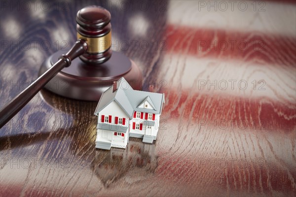 Small house and gavel on wooden table with american flag reflection