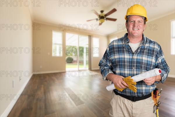 Contractor with plans and hard hat inside empty room with wood floors