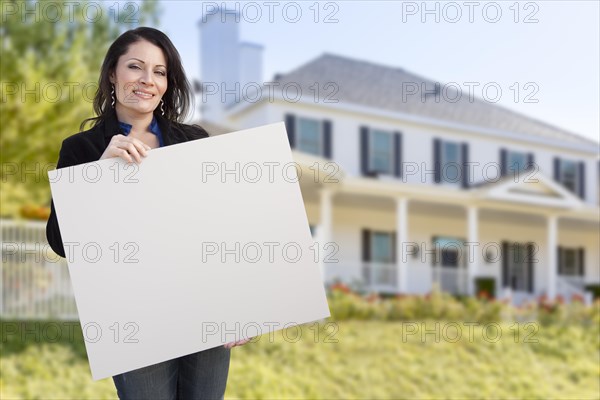 Smiling hispanic female holding blank sign in front of beautiful house