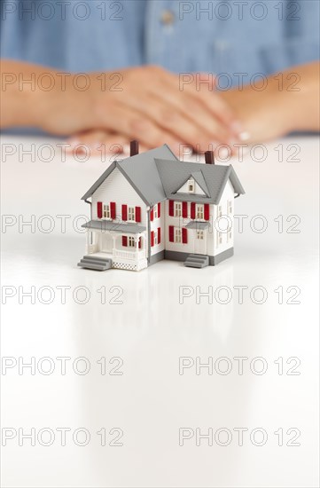 Womans folded hands behind model house on white surface