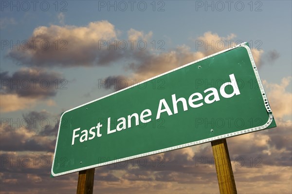 Fast lane ahead green road sign over dramatic clouds and sky