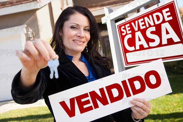Happy attractive hispanic woman holding vendido real estate sign and keys in front se vende casa real estate sign and house