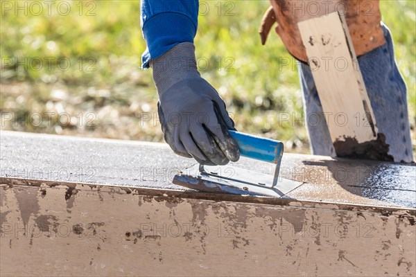 Construction worker using hand groover on wet cement forming coping around new pool