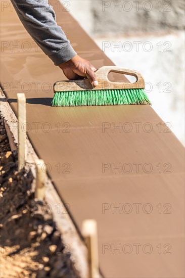 Construction worker using brush on wet cement forming coping around new pool