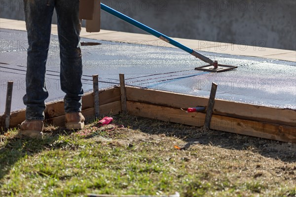 Construction worker smoothing wet cement with long handled edger tool