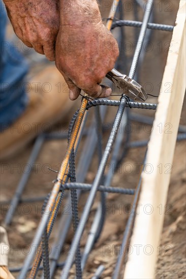 Worker securing steel rebar framing with wire plier cutter tool at construction site