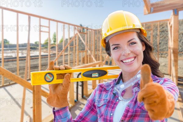 Female construction worker with thumbs up holding level wearing gloves