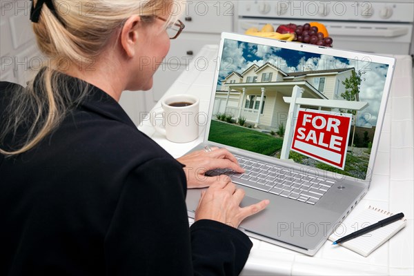 Woman in kitchen using laptop to research real estate. screen can be easily used for your own message or picture. picture on screen is my copyright as well