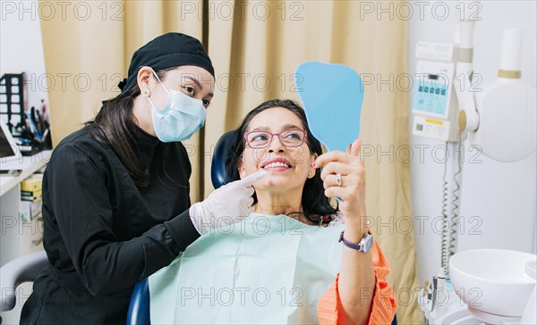 Satisfied female client in dental clinic looking at mirror