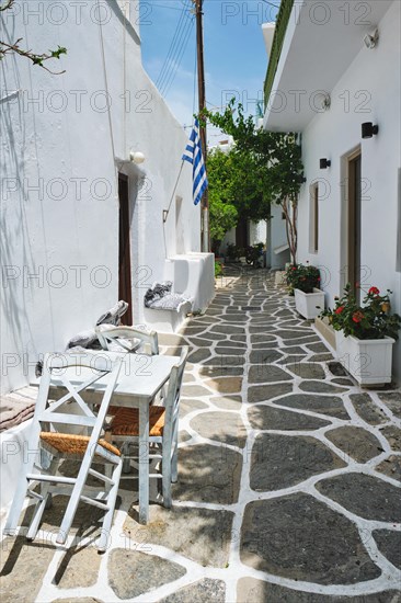 Picturesque narrow street with traditional whitewashed houses with greek flag and cafe tables in Naousa town in famous tourist attraction Paros island