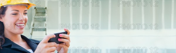 Female contractor wearing hard hat using cell phone against dywall banner background with ladder