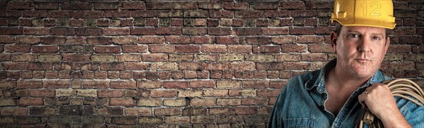 Male contractor in hard hat holding cable in front of old brick wall banner with copy space