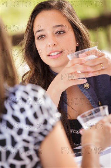 Expressive young adult woman having drinks and talking with her friend outdoors