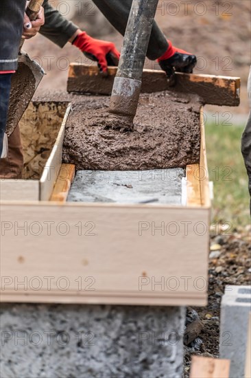 Construction workers pouring and leveling wet cement into wood framing