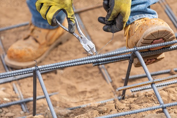 Worker securing steel rebar framing with wire plier cutter tool at construction site