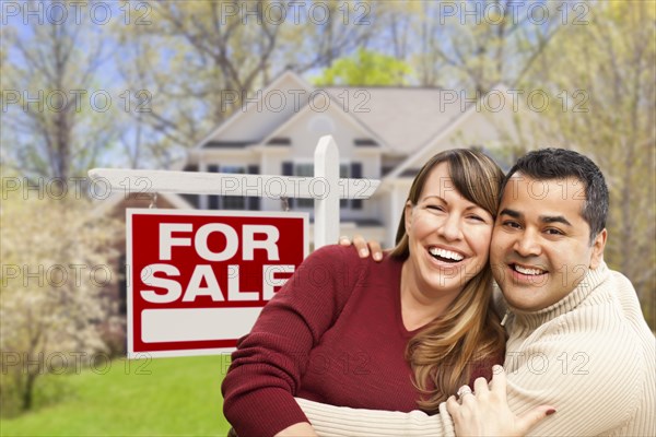 Happy couple in front of for sale real estate sign and new house