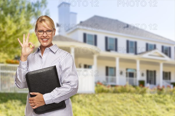 Attractive businesswoman with okay hand sign in front of nice residential home