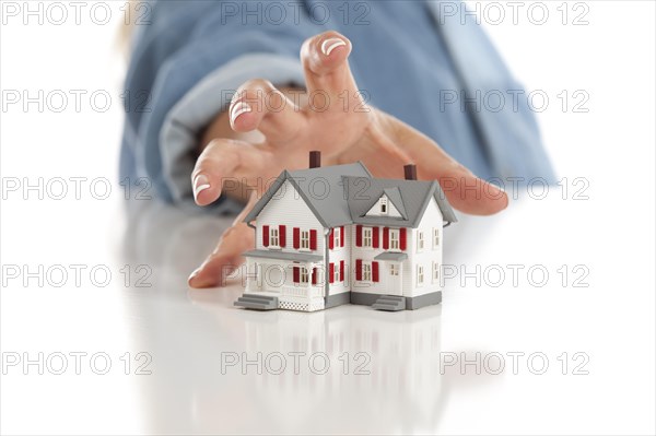 Womans hand reaching for model house on a white surface