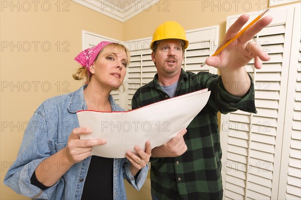 Male contractor in hard hat discussing plans with woman in room