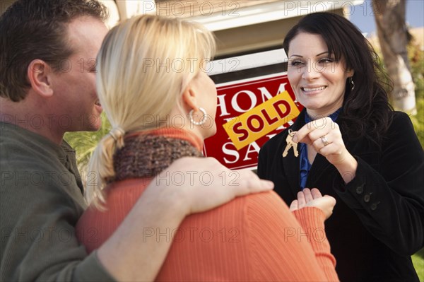 Attractive hispanic female real estate agent handing over new house keys to happy couple