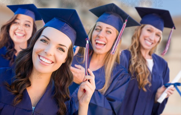 Happy graduating group of girls in cap and gown celebrating on campus