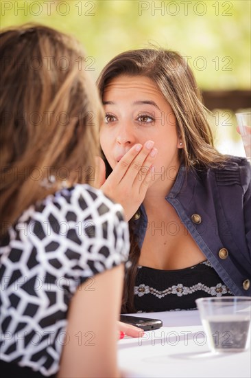 Expressive young adult woman having drinks and talking with her friend outdoors