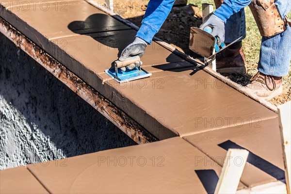 Construction worker using hand groover on wet cement forming coping around new pool