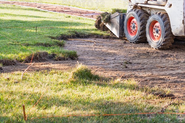 Small bulldozer removing grass from yard preparing for pool installation