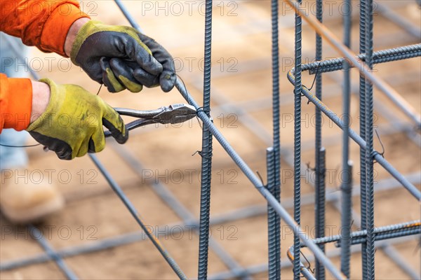 Worker securing steel rebar framing with wire plier cutter tool at construction site