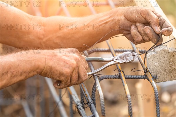 Worker securing steel rebar framing with wire plier cutter tool at construction site